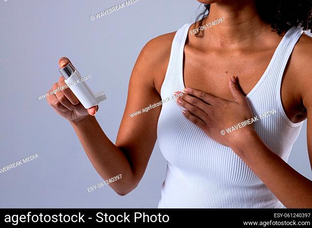 Midsection of african american mid adult woman holding asthma inhaler against white background