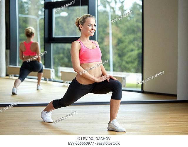 fitness, sport, training, gym and lifestyle concept - smiling woman stretching leg in gym