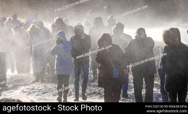 dpatop - 30 January 2022, Mecklenburg-Western Pomerania, Rostock: Onlookers walk through the sandstorm on the pier of Warnemünde