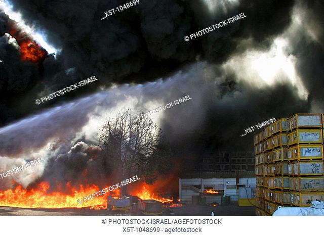 Israel, Galilee, a raging wild fire in an agricultural packing plant  A jet of water from the left is aimed at the flames