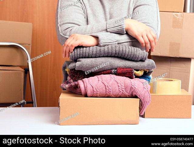 woman in a gray sweater is packing clothes in a box, the concept of assistance and volunteering, moving. Selling unnecessary things