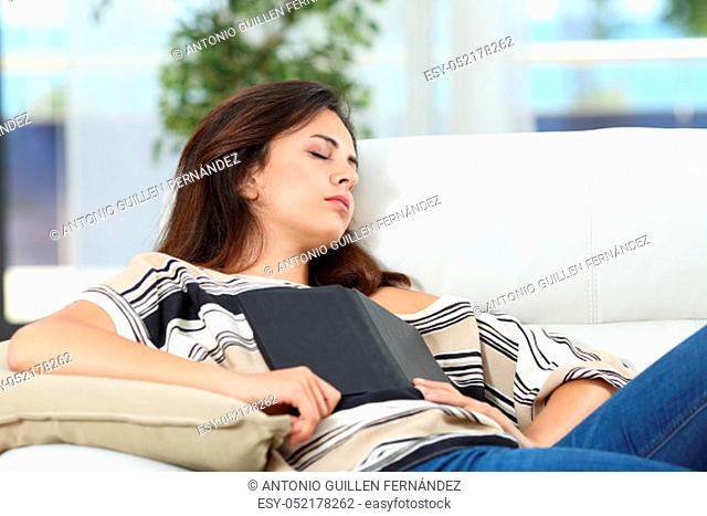 Relaxed woman is sleeping holding an ebook lying on a couch at home
