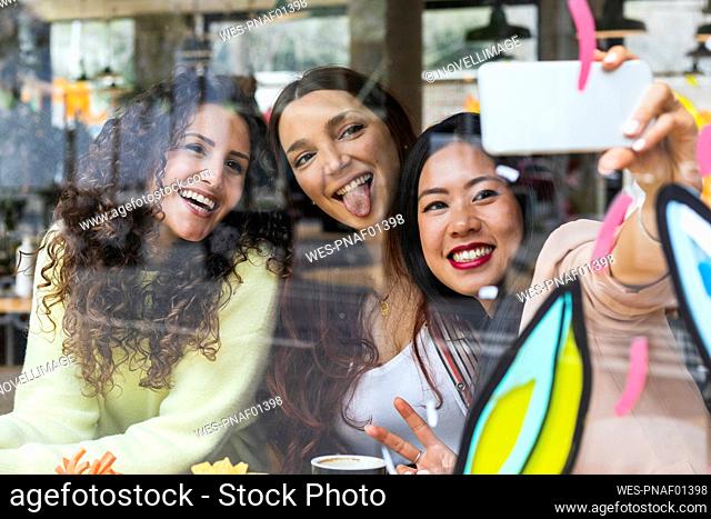 Cheerful friends taking selfie through mobile phone at cafe