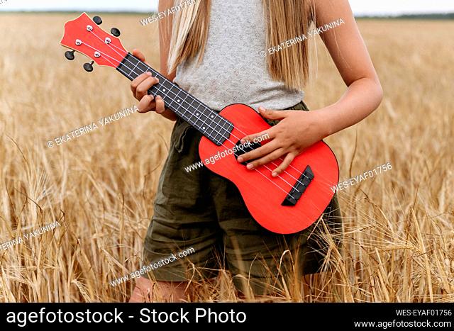 Girl playing guitar while standing on wheat field