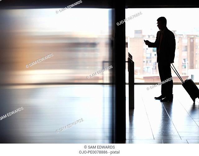 Businessman pulling luggage and using cell phone