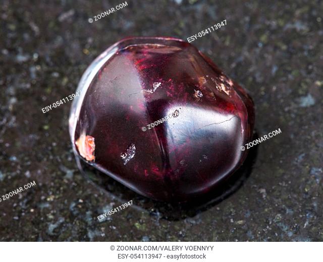 macro shooting of natural mineral rock specimen - polished red garnet gemstone on dark granite background