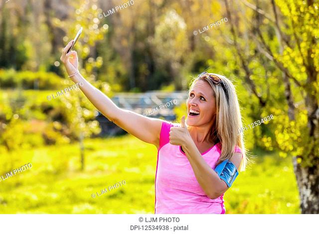 A mature woman wearing active wear and an arm band to hold her smart phone takes a self-portrait before heading out for a run in a city park during the fall...