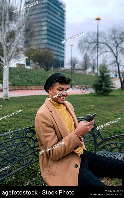 Smiling young man sitting on a bench using cell phone