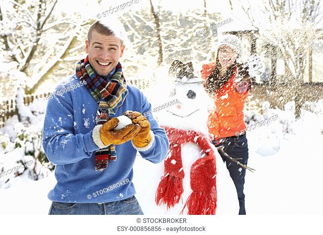 Young Couple Having Snowball Fight In Garden