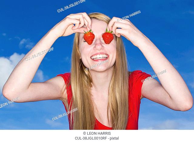 Woman holding strawberries over eyes