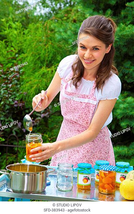 A young woman filling jars with apricot jam