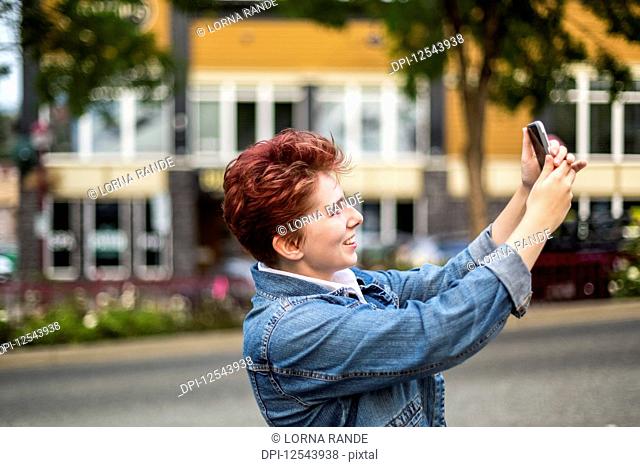 A teenage girl with red hair taking a self-portrait with a smart phone; Abbotsford, British Columbia, Canada