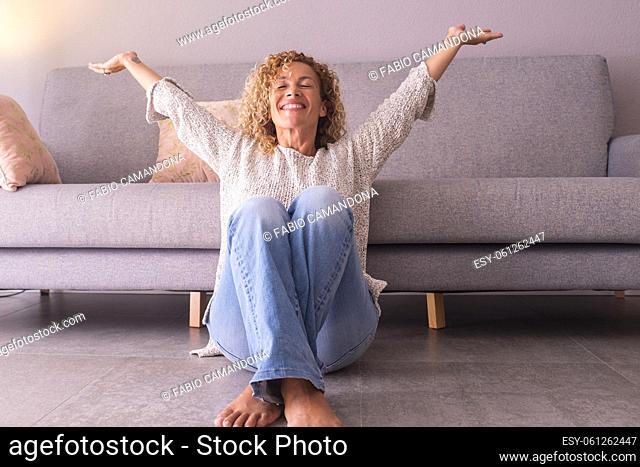 Happy and satisfied woman at home sitting on the floor opening arms and smiling. Concept of joyful lifestyle female people