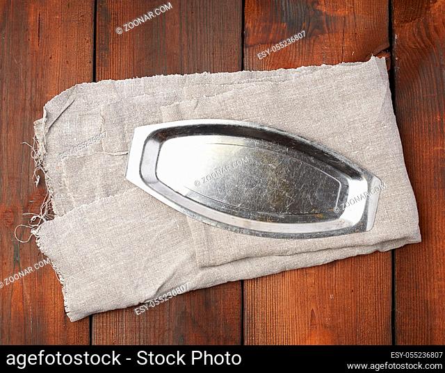 iron empty plate on a gray textile napkin, brown wooden background, top view