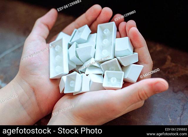 top view closeup of Caucasian child hands holding many pbt keycaps of a white mechanical keyboard in natural lighting