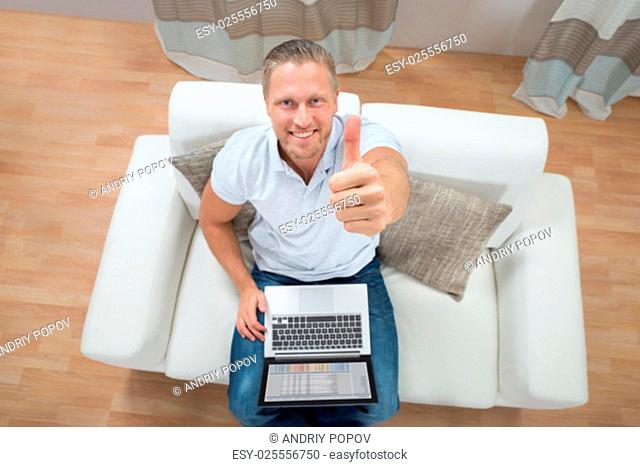 Young Happy Man On Sofa Showing Thumb Up With Laptop