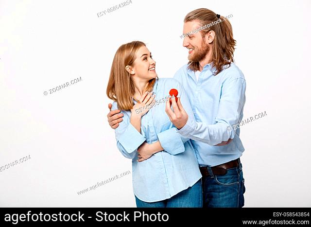Proposal concept - Portrait of man showing an engagement ring diamond to his beutiful girlfriend over isolated white background