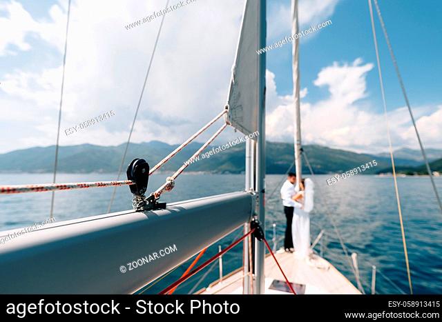 View from the bow of a sailing yacht. Newlyweds stand at the stern of a sailboat against the backdrop of mountains. High quality photo