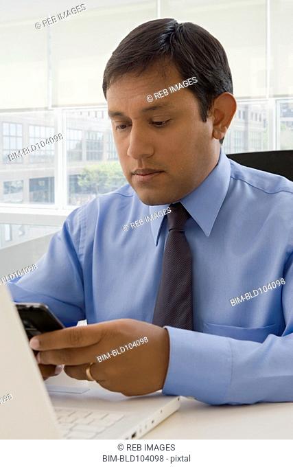 Hispanic businessman using cell phone at desk