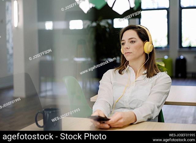 Woman listening music while sitting by table in office