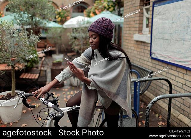 Young woman with smart phone on bicycle outside sidewalk cafe