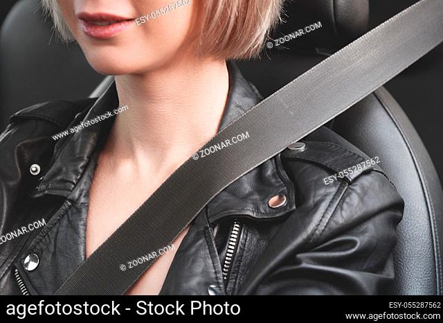 A close-up of a young hipster girl in a leather jacket in a car fastened with a seat belt. The concept of safety and protection of the driver on the road