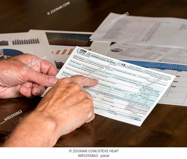 Senior hand holding Form 1040 Simplified for 2018 which allows for filing on April 15, tax day, on a postcard