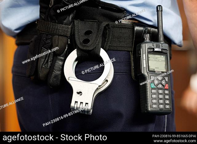 16 August 2023, North Rhine-Westphalia, Detmold: A view of gloves, handcuffs and a court officer's walkie-talkie in Detmold District Court