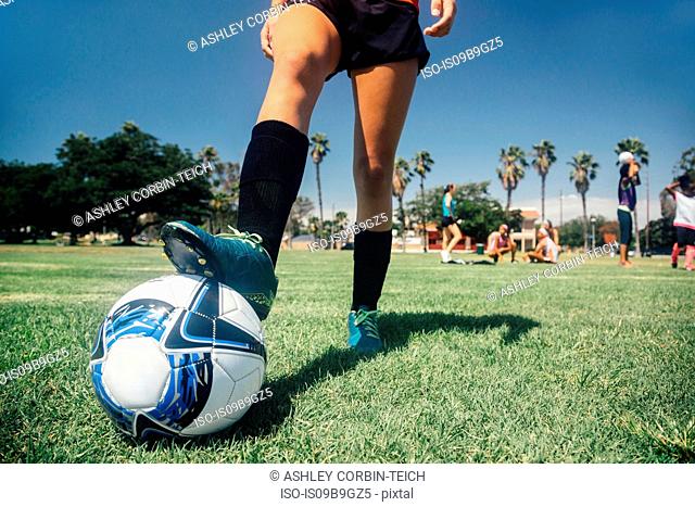 Waist down of teenage schoolgirl soccer player with foot on ball on school sports field