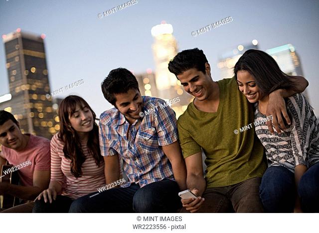 A small group of friends gathered on a rooftop terrace overlooking a city at twilight