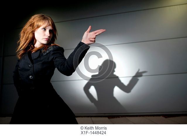 A late teen early 20s single woman girl with red hair pointing her fingers like a gun, casting shadow, UK