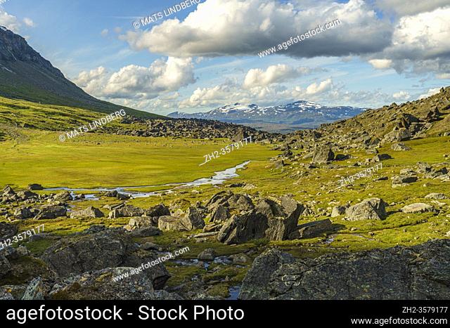 Hiking trail at Kärkevagge, Swedish Lapland with big rocks and river floating and mountains in background and cloudy weather, Kiruna county, Swedish Lapland