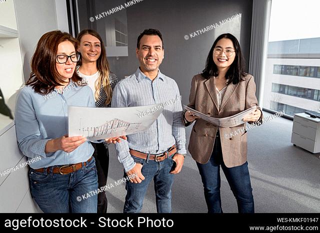 Confident business people standing in office holding architectural plans