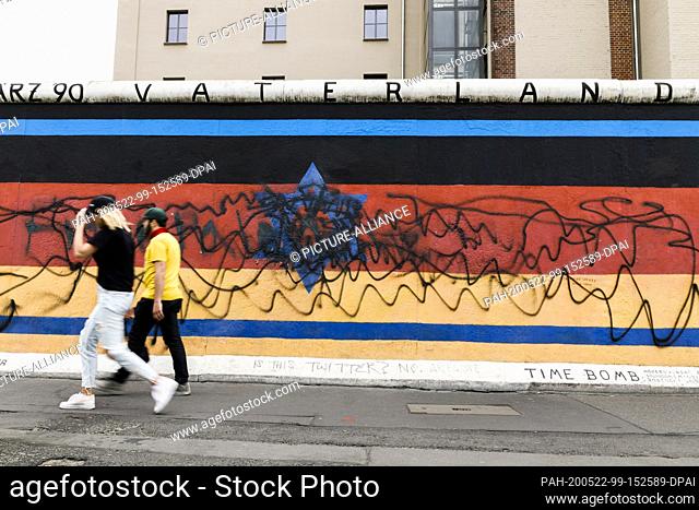 22 May 2020, Berlin: Passers-by walk past the destroyed mural by the artist Günther Schäfer at the East Side Gallery. The mural ""Vaterland""
