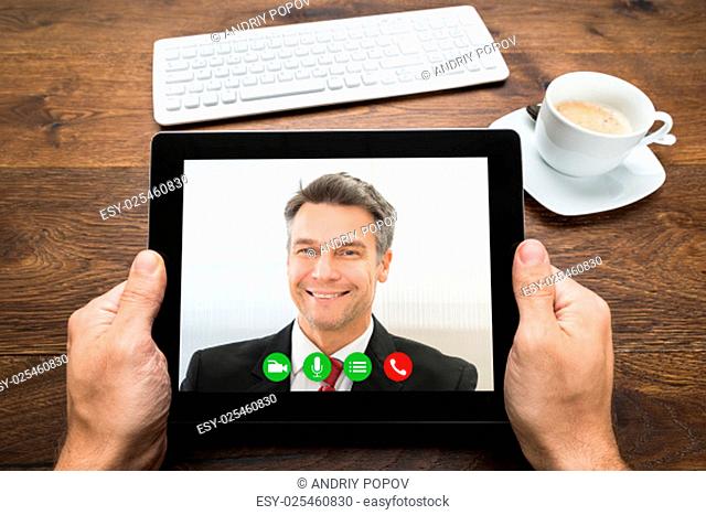 Close-up Of Businessperson Video Chatting With Colleague On Digital Tablet At Desk