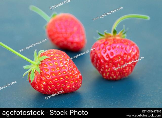 Drei reife Erdbeeren auf taubenblauem Untergrund