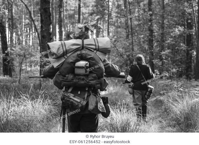 Re-enactors Dressed As German Infantry Soldiers In World War II Marching Walking Along Forest Road In Summer Day. Photo In Black And White Colors