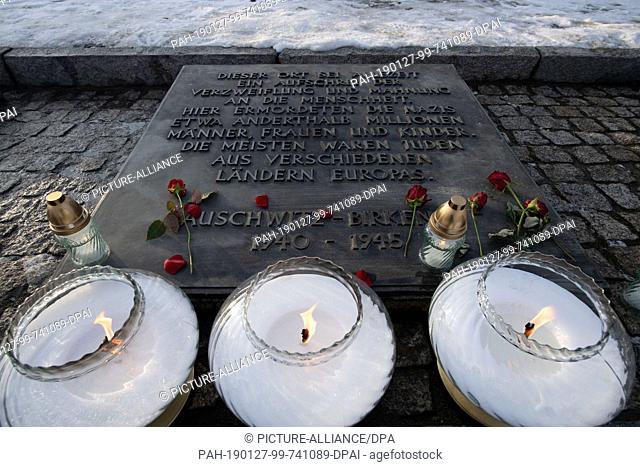 27 January 2019, Poland, Oswiecim: Candles are lit in front of a commemorative plaque in German for the people imprisoned in the former Auschwitz-Birkenau...