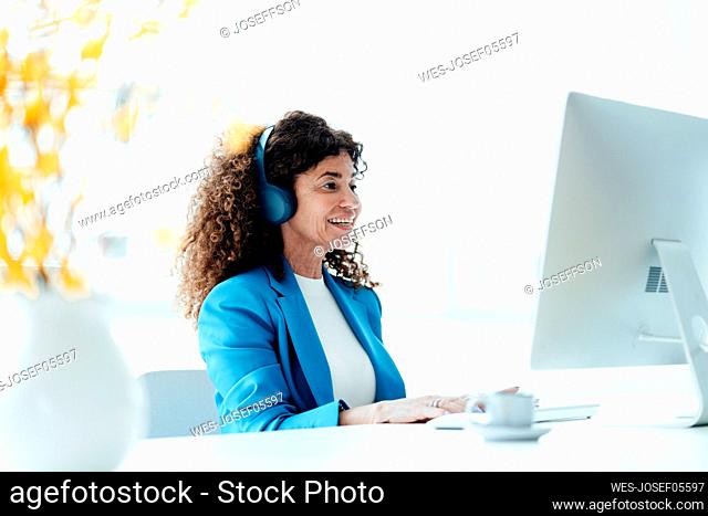 Mature businesswoman wearing headphones while working at desk in office