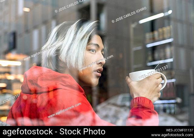 Asian man looking through glass while having coffee in cafe