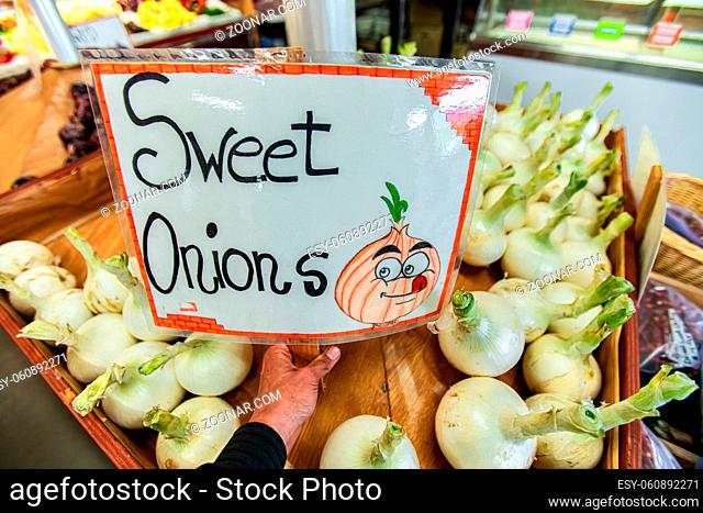 Sweet onions on sale at the local food market. Hand written plasticized signboard. Drawing of happy and smiling onion with tongue sticking out