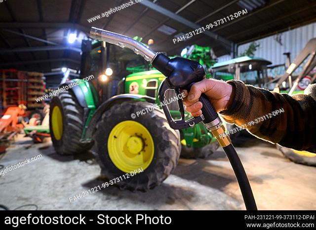 21 December 2023, Lower Saxony, Hanover: A farmer in the Hanover region holds a nozzle of his diesel tank in front of a tractor in his vehicle shed