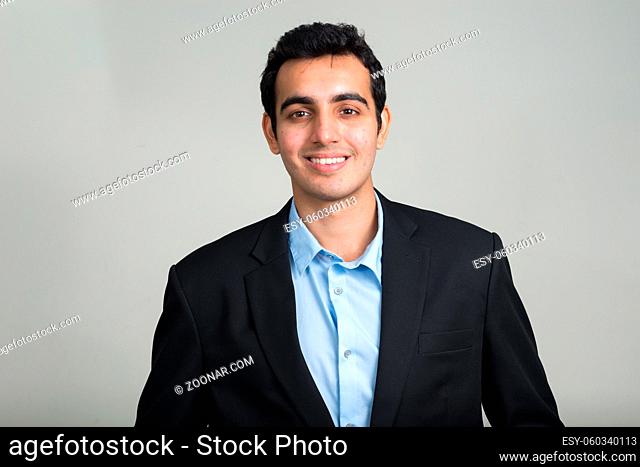 Studio shot of young handsome Indian businessman in suit against white background