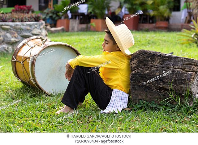 Young boy in Farmer's clothing hat covering his face sleeping sitting next to a drum