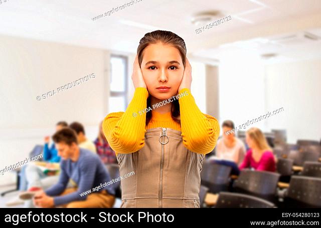 student girl closing ears by hands at school