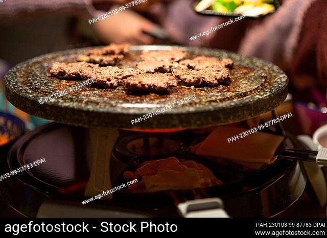 PRODUCTION - 31 December 2022, North Rhine-Westphalia, Bergheim: During a raclette meal on New Year's Eve, minced meat is frying on the stone plate of a...