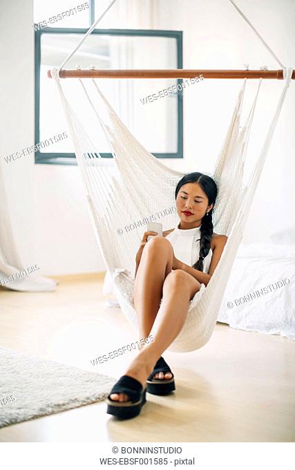Young woman sitting in hammock using cell phone