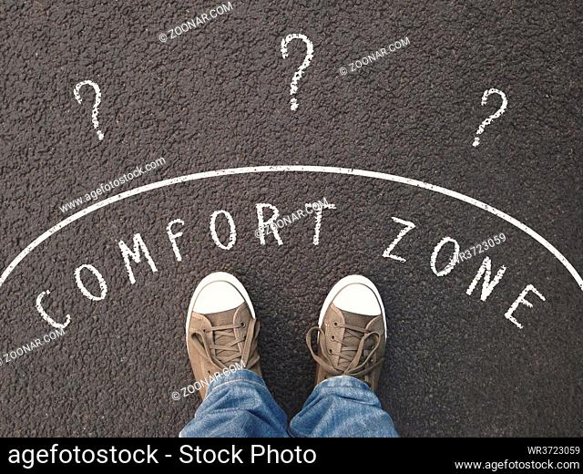 feet of unrecognizable person standing on street with chalk text on asphalt - leaving comfort zone concept