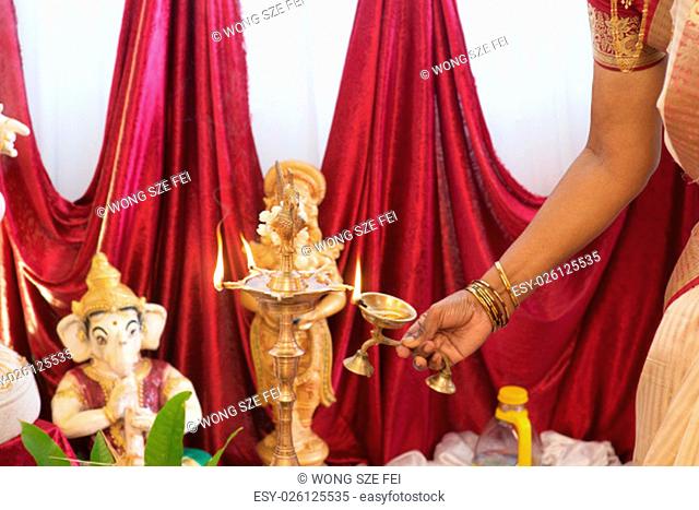Woman hand lighting up the metal diya. Traditional Indian Hindus religious ceremony. Focus on the oil lamp. India special rituals events