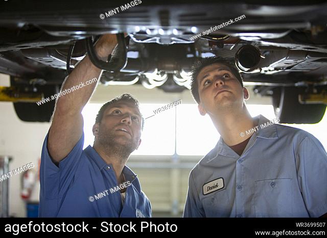 Two mechanics work on the underside of a car on a lift in a repair shop